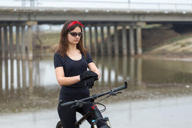 Ragazza su una mountain bike su fuoristrada bellissimo ritratto di un ciclista in tempo piovoso Ragazza fitness guida una moderna mountain bike in fibra di carbonio in abbigliamento sportivo Ritratto del primo piano di una ragazza in bandana rossa