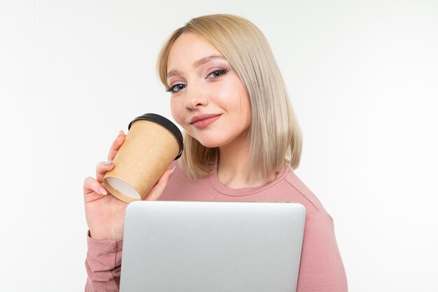 Ragazza su una pausa caffè con una tazza di caffè e un computer portatile in sue mani su una priorità bassa bianca