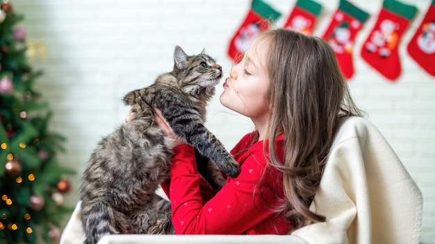 Ragazza su una sedia con un gatto a casa, albero di Natale sul muro