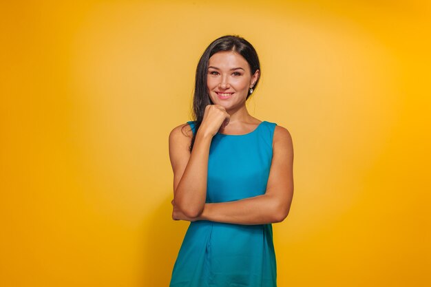 Ragazza su uno sfondo giallo in un vestito blu, tenendo la mano sul viso