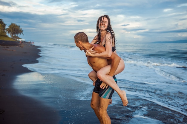 Ragazza sulla schiena di un uomo sulla schiena alla spiaggia