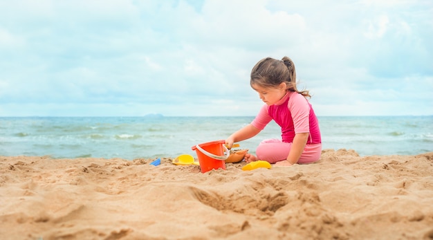 Ragazza sulla spiaggia che gioca nella sabbia. bambino in costume da bagno rosa che riposa sulla spiaggia