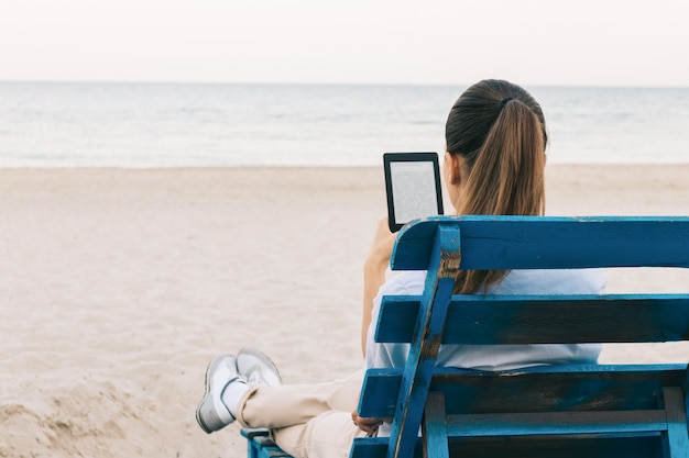 Ragazza sulla spiaggia leggendo un libro seduto sulla panchina