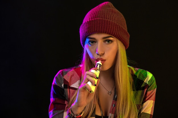 Ragazza svapata. Giovane donna hipster vape e-cig in studio su sfondo nero. Stile hip-hop. Avvicinamento.