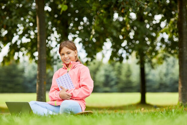 Ragazza sveglia che per mezzo del computer portatile all'aperto