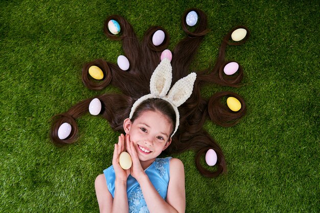 Ragazza sveglia che si trova sull'erba con le uova di Pasqua. Le uova di Pasqua sono tra i capelli.