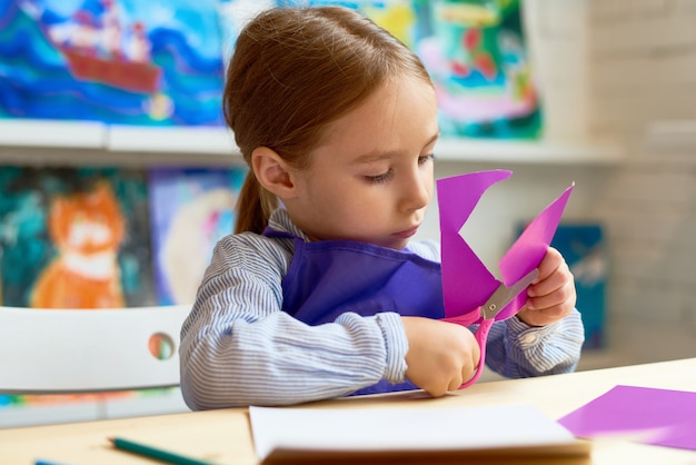 Ragazza sveglia che taglia cuore di carta nella classe del mestiere