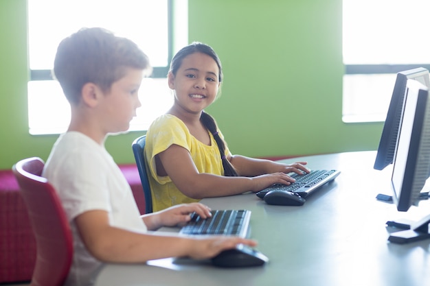 Ragazza sveglia con il compagno di classe maschio che per mezzo del computer