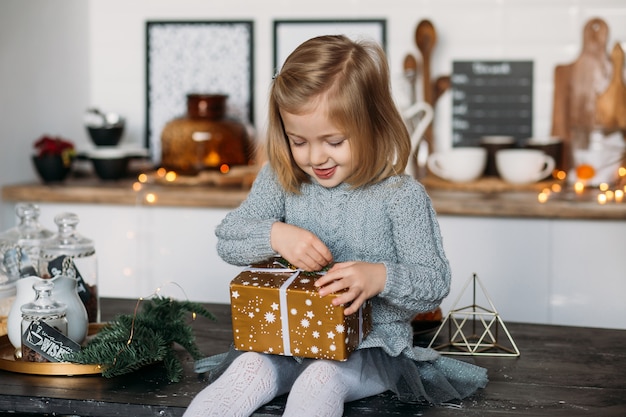 Ragazza sveglia con il contenitore di regalo di natale in cucina. Buon Natale e Buone Feste!