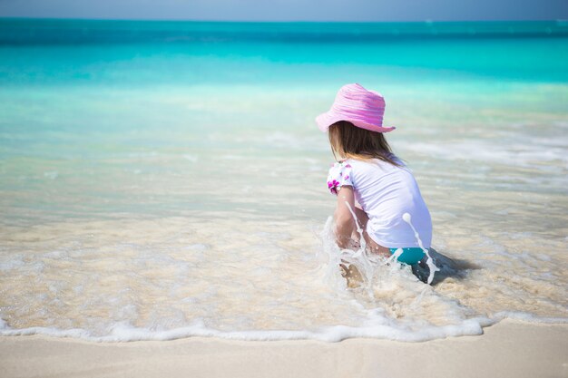 Ragazza sveglia del bambino che gioca in acque basse alla spiaggia esotica