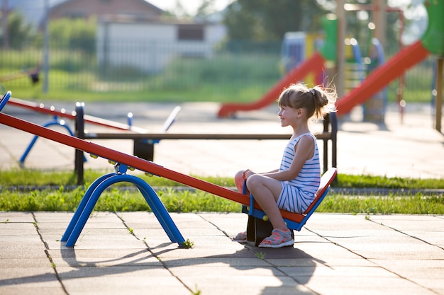 Ragazza sveglia del bambino piccolo all'aperto sull'oscillazione della sega il giorno di estate soleggiato