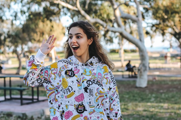 Ragazza sveglia dell'adolescente che saluta gli amici all'aperto. Ragazza della scuola agitando la mano ai suoi amici