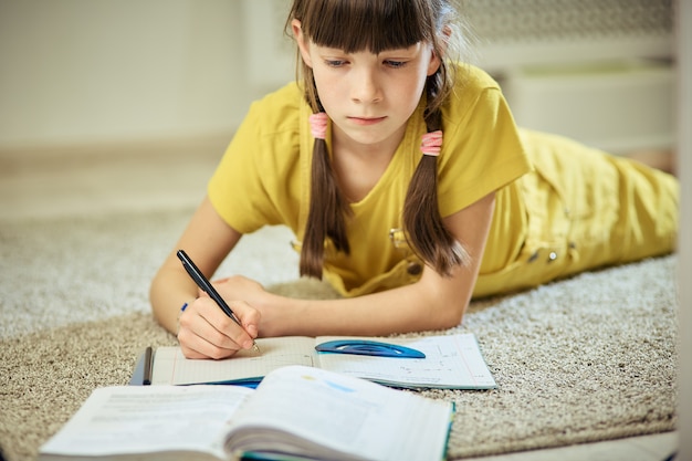 Ragazza teen facendo i compiti seduti sul tappeto nella sua stanza