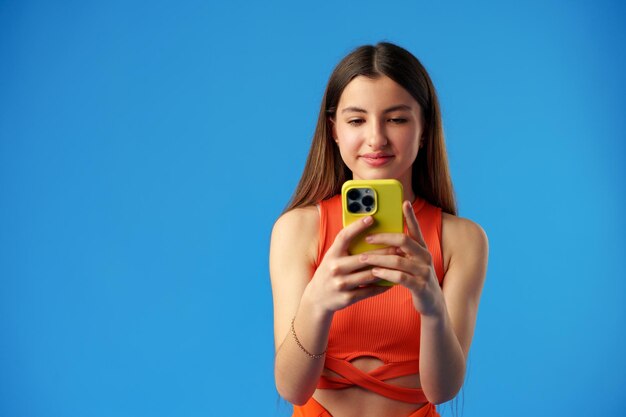 Ragazza teenager alla moda che utilizza smartphone su sfondo blu