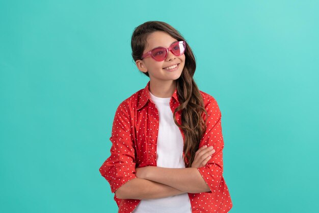 Ragazza teenager allegra che distoglie lo sguardo con lunghi capelli ricci in occhiali da sole e camicia casual alla moda