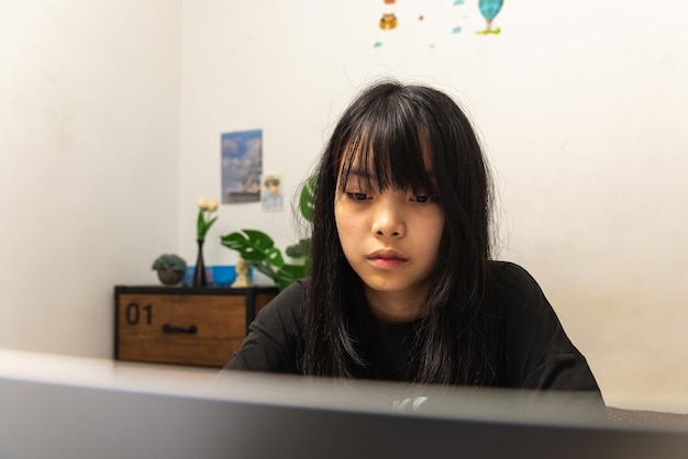 Ragazza teenager asiatica usa il computer portatile tecnologia internet ricerca online informazioni social network e istruzione compiti sul tavolo