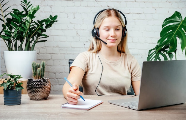 Ragazza teenager bionda che indossa le cuffie che studia in linea con l'insegnante di skype della chat di Internet