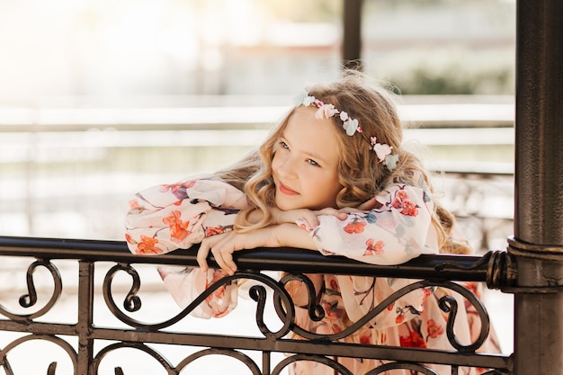 Ragazza teenager bionda sorridente che posa nel giardino estivo Indossando una corona di fiori all'aperto