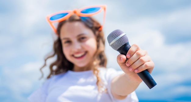 Ragazza teenager che canta una canzone nel microfono sulla musica del karaoke del fondo del cielo
