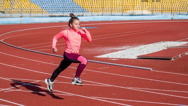 Ragazza teenager che corre sulla maratona della pista da corsa dello stadio all'aperto