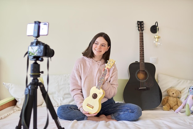 Ragazza teenager che gioca sull'ukulele. Blog, canale musicale, vlog, ragazza che studia online, parla con i follower e suona musica