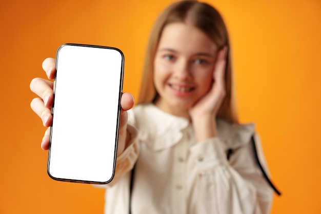 Ragazza teenager che mostra lo schermo dello smartphone con spazio per la copia su sfondo giallo