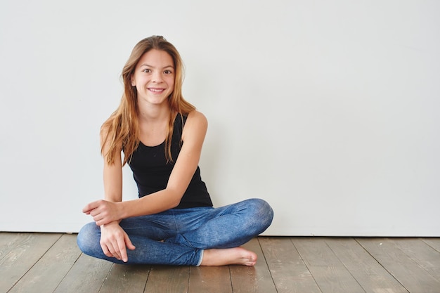 Ragazza teenager che si siede su un pavimento di legno contro un fondo bianco