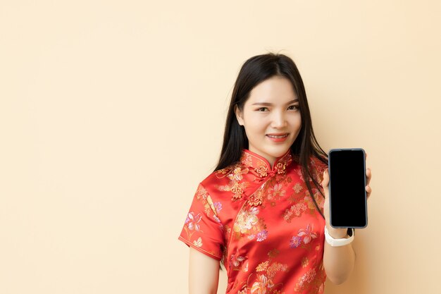 Ragazza teenager cinese che mostra lo schermo in bianco dello Smart Phone che veste il panno tradizionale di Qipao.