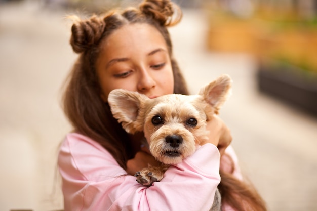 Ragazza teenager con il piccolo cane animale da compagnia che tiene in mani all'aperto in un parco.