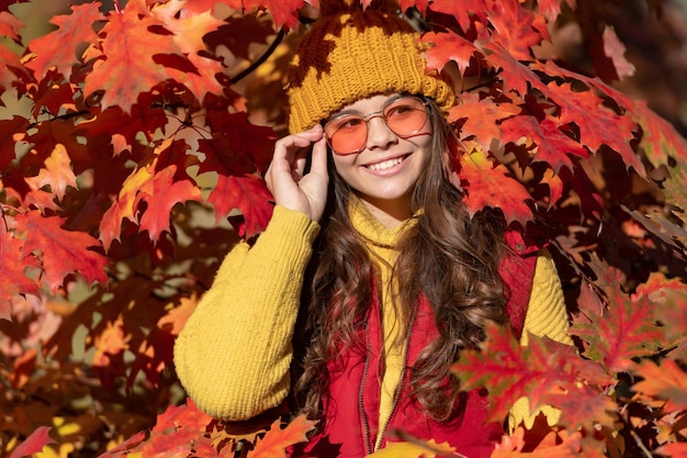 Ragazza teenager del bambino sulla caduta di autunno lascia il capretto positivo in occhiali da sole alle foglie di autunno su sfondo naturale