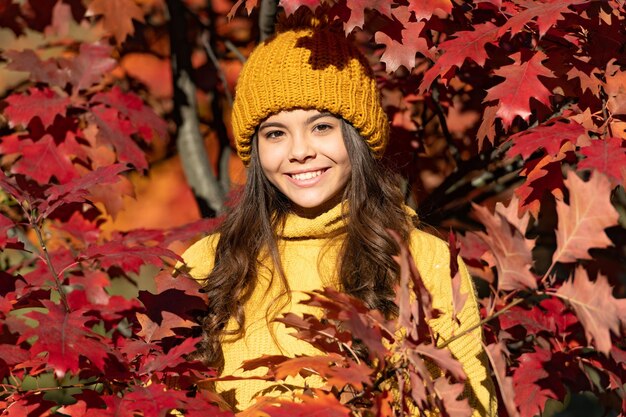 Ragazza teenager del bambino sulla caduta di autunno lascia il fondo faccia felice del bambino nel cappello alle foglie di autunno su fondo naturale