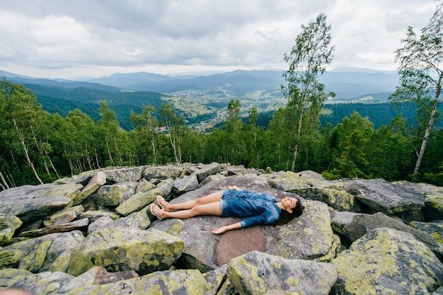 Ragazza teenager del Brunette che si trova sulle pietre in cima alla montagna