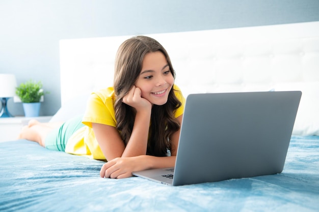 Ragazza teenager della scuola che studia a casa sul letto con il computer portatile