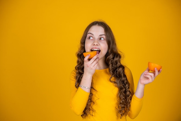 Ragazza teenager felice che mangia frutta arancione su fondo giallo
