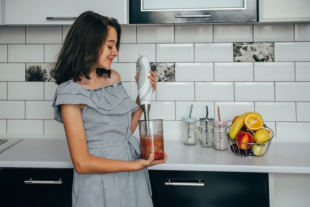 Ragazza teenager felice che produce succo fresco o pasto in un frullatore in cucina.