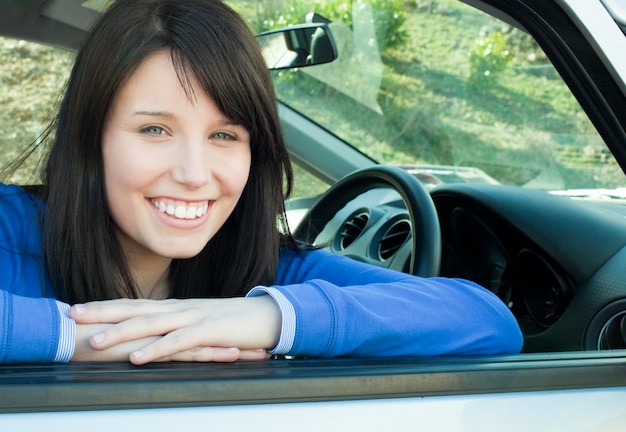 Ragazza teenager felice che sorride alla macchina fotografica che si siede nella sua automobile