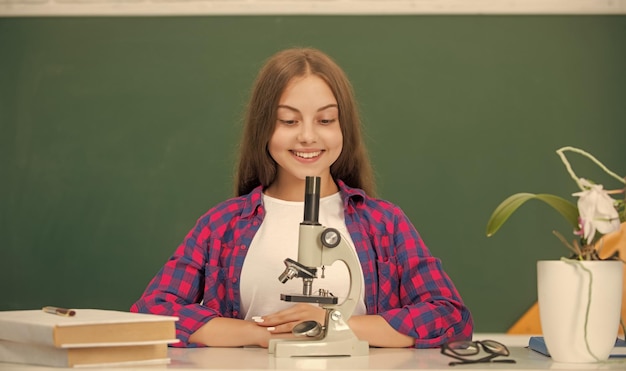 Ragazza teenager felice che usa il microscopio per tornare a studiare il laboratorio di chimica della biologia