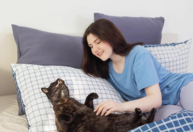 Ragazza teenager felice con il gatto nero in camera da letto bianca
