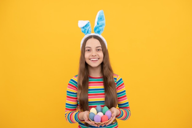 Ragazza teenager felice di pasqua nelle orecchie del coniglietto del coniglio che tiene le uova dipinte per la caccia del coniglietto di caccia delle uova di festa