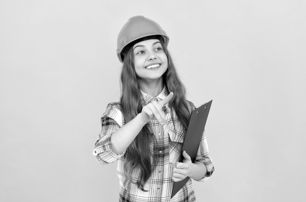 Ragazza teenager felice in casco e camicia a scacchi che prende appunti sugli appunti occupati