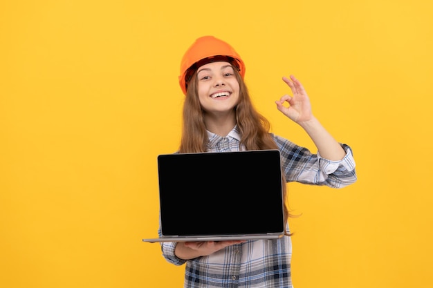 Ragazza teenager felice in casco e camicia a scacchi che presenta laptop, ok.