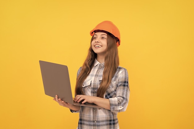 Ragazza teenager felice in casco e camicia a scacchi usando la scuola del computer portatile