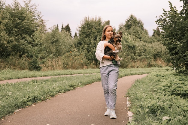 Ragazza teenager in una passeggiata nel parco estivo con il suo animale domestico Yorkshire terrier. Bambino che porta a spasso un cane