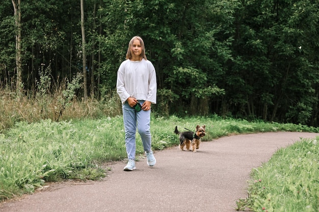 Ragazza teenager in una passeggiata nel parco estivo con il suo animale domestico Yorkshire terrier. Bambino che porta a spasso un cane