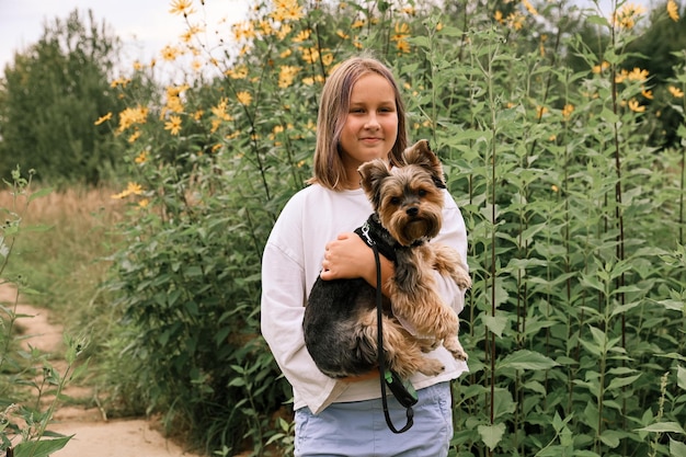 Ragazza teenager in una passeggiata nel parco estivo con il suo animale domestico Yorkshire terrier. Bambino che porta a spasso un cane