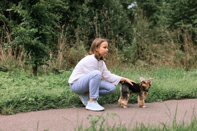 Ragazza teenager in una passeggiata nel parco estivo con il suo animale domestico Yorkshire terrier. Bambino che porta a spasso un cane