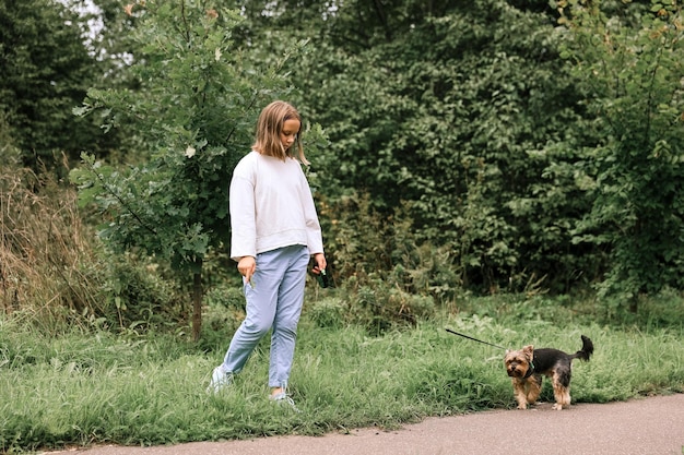 Ragazza teenager in una passeggiata nel parco estivo con il suo animale domestico Yorkshire terrier. Bambino che porta a spasso un cane