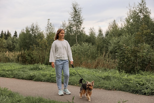 Ragazza teenager in una passeggiata nel parco estivo con il suo animale domestico Yorkshire terrier. Bambino che porta a spasso un cane