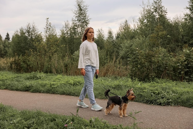 Ragazza teenager in una passeggiata nel parco estivo con il suo animale domestico Yorkshire terrier. Bambino che porta a spasso un cane