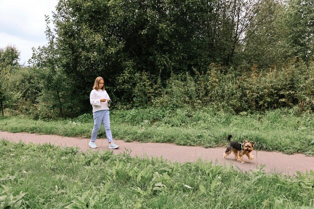 Ragazza teenager in una passeggiata nel parco estivo con il suo animale domestico Yorkshire terrier. Bambino che porta a spasso un cane